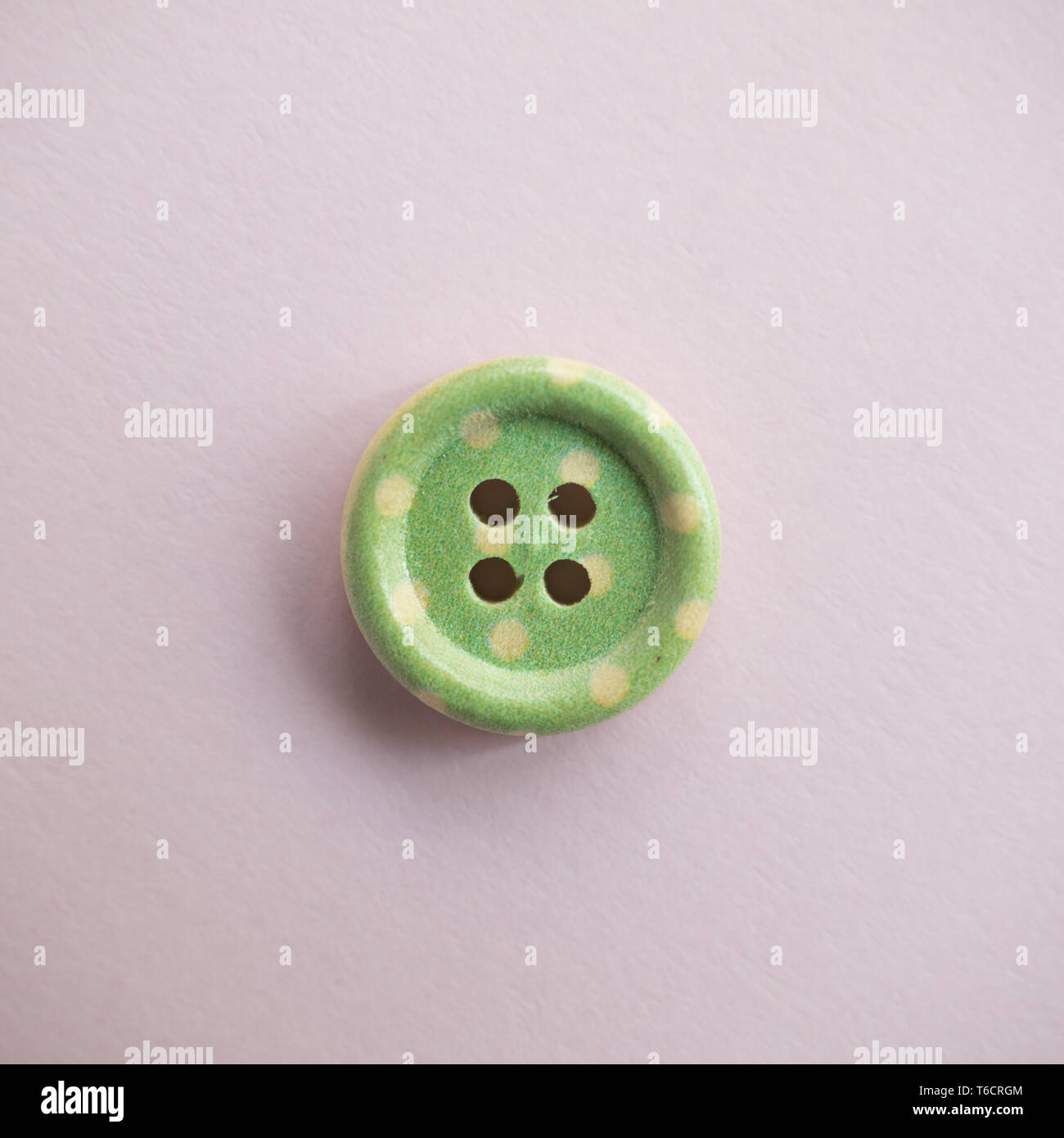 Isolated wooden button with colored colorful dots on a light pink background, sewing Stock Photo