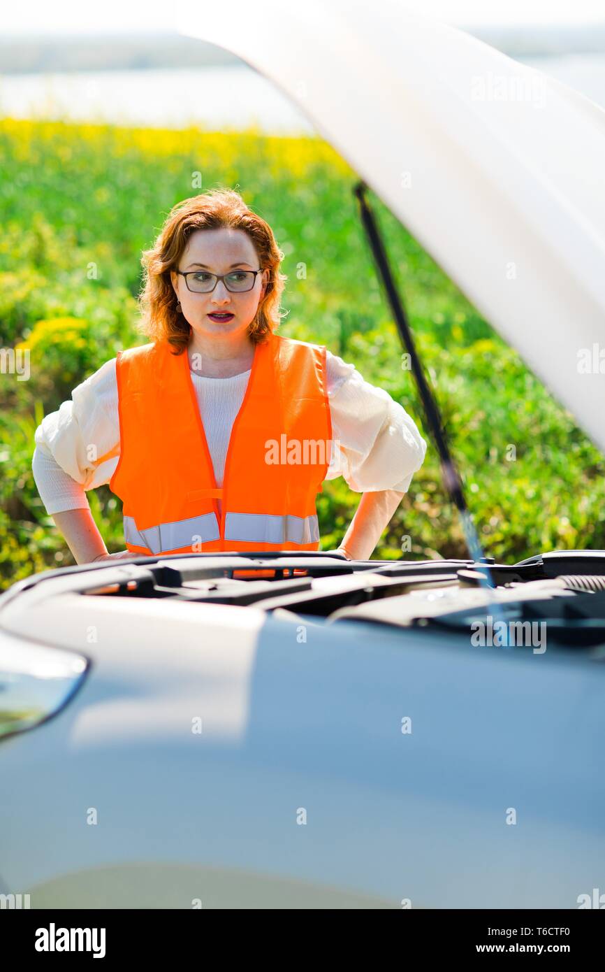 A woman in orange vest open car bonnet of broken car - trying to solve problem Stock Photo