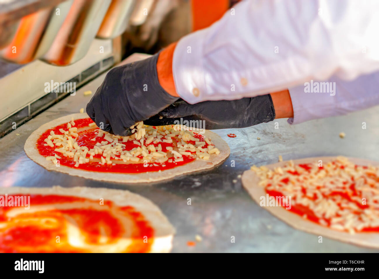 Pizza maker preparing a margherita pizza sprinkling diced mozzarella cheese on a pasta base already seasoned with tomato sauce and ready to bake. Ital Stock Photo