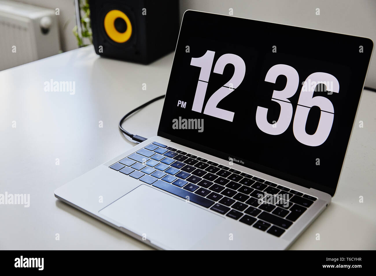 Apple MacBook Pro notebook with the clock screensaver on the big white Ikea desk office with the black yellow speakers, iPhone in the background Stock Photo