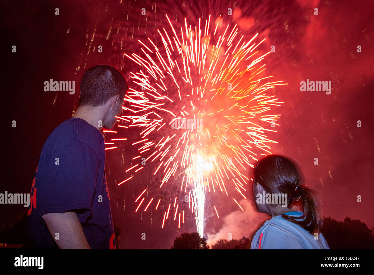 Brother and sister watch fireworks exploding in the night sky. Stock Photo