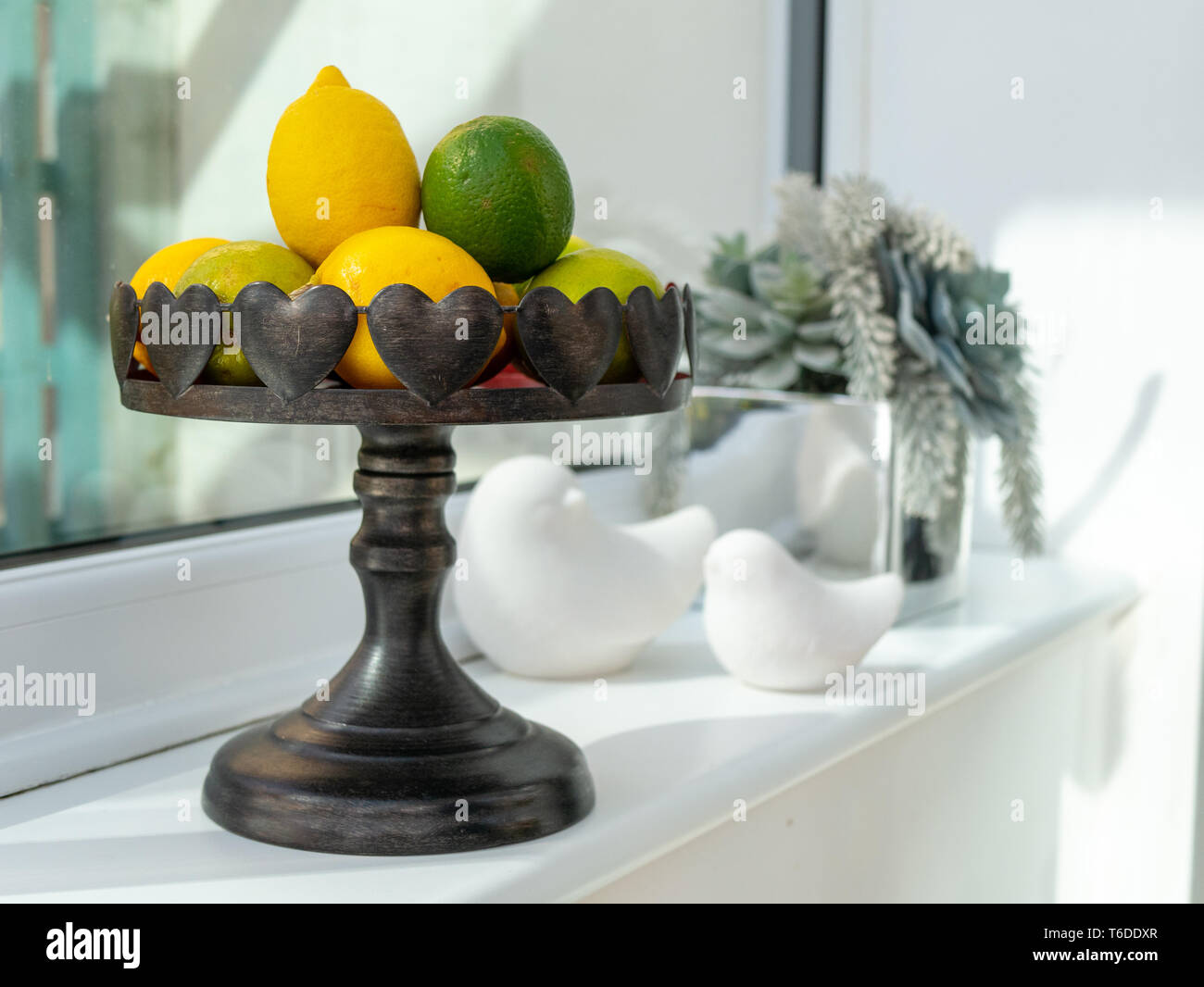 lemons and limes in a bowl on neutral windowsill Stock Photo