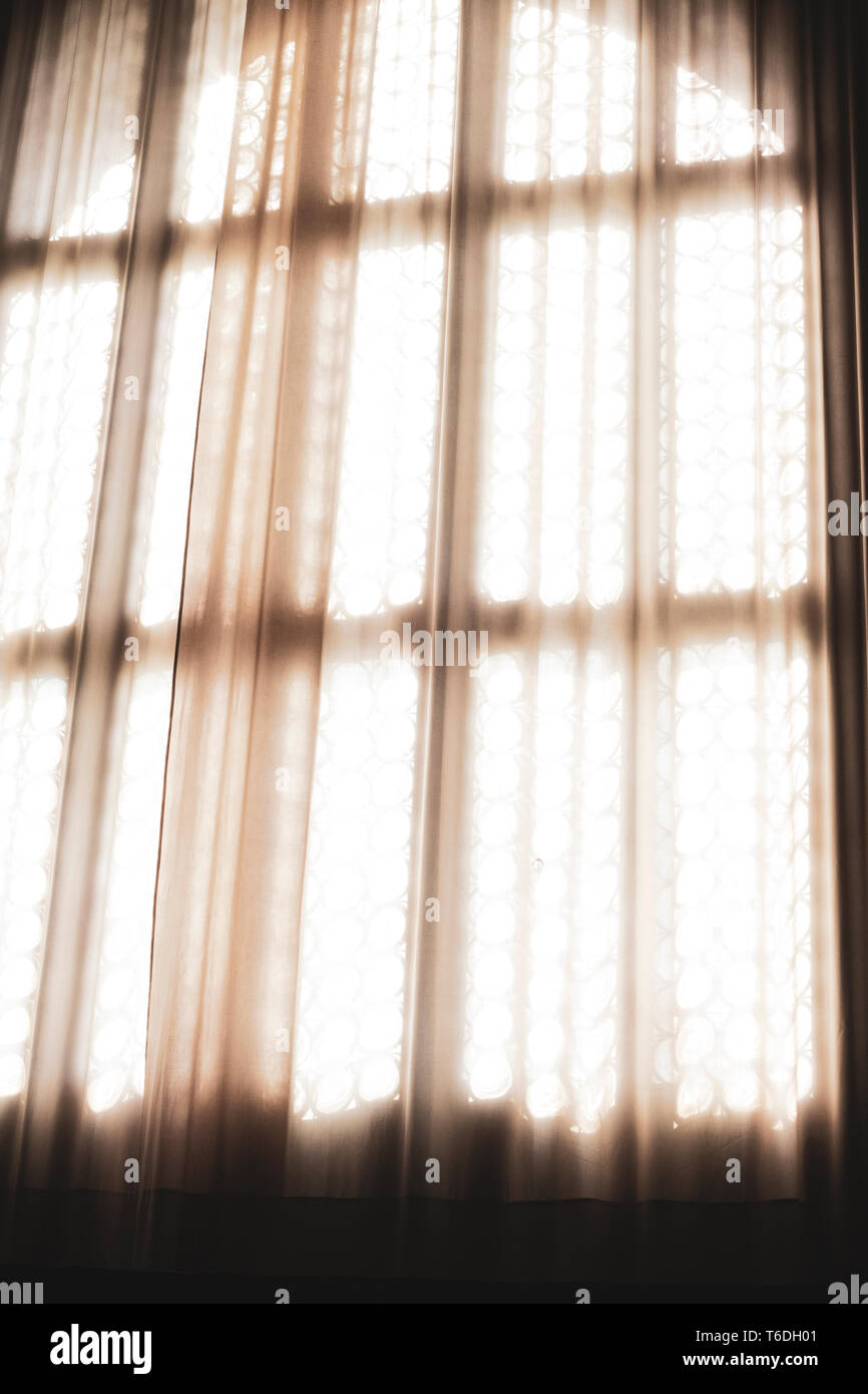 Close up of sunlight filtering through a net curtain in front of leaded glass window. Stock Photo