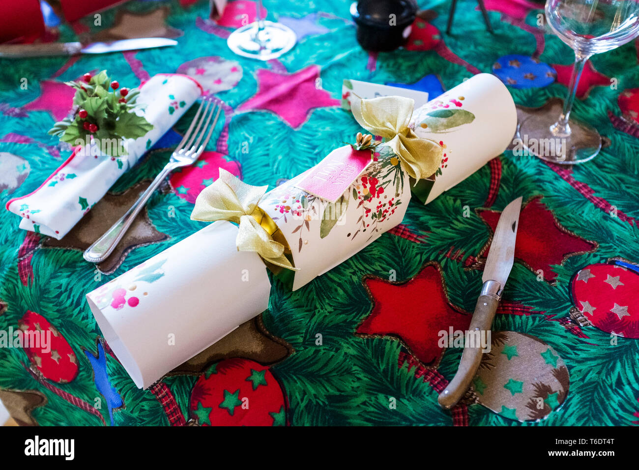 High angle close up of cutlery and white Christmas cracker on green and red table cloth with Christmas motifs. Stock Photo