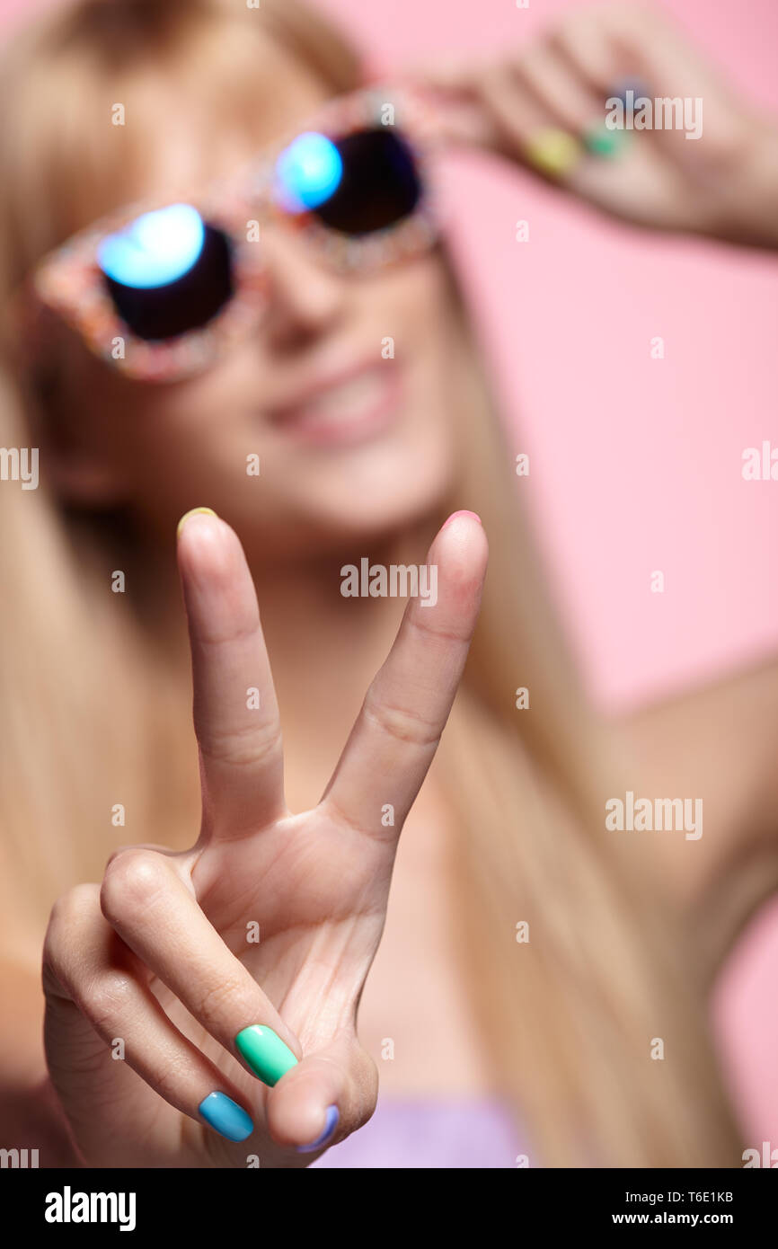 Female portrait with shallow depth of focus. Young blonde smiling  woman with fun candy glasses and sign of victory Stock Photo
