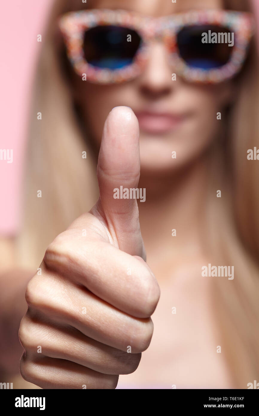 Female portrait with shallow depth of focus. Young blonde smiling  woman with fun candy glasses and thumb up Stock Photo