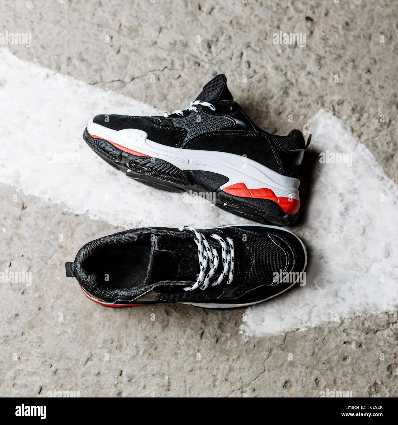 black sneakers with white laces on a thick white sole with red accents on a  concrete background near a painted white arrow Stock Photo - Alamy