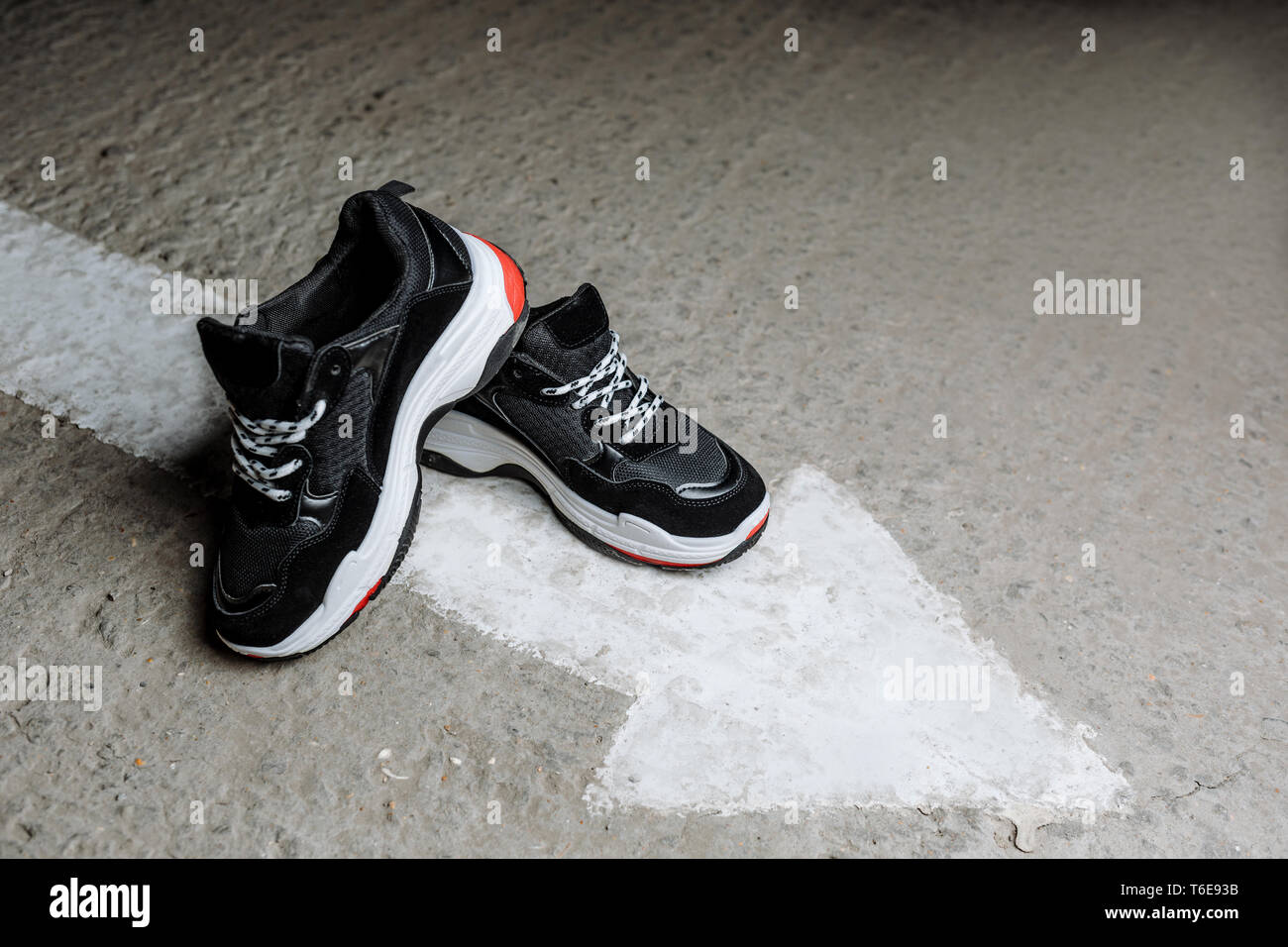 black sneakers with white laces on a thick white sole with red accents on a  concrete background near a painted white arrow Stock Photo - Alamy