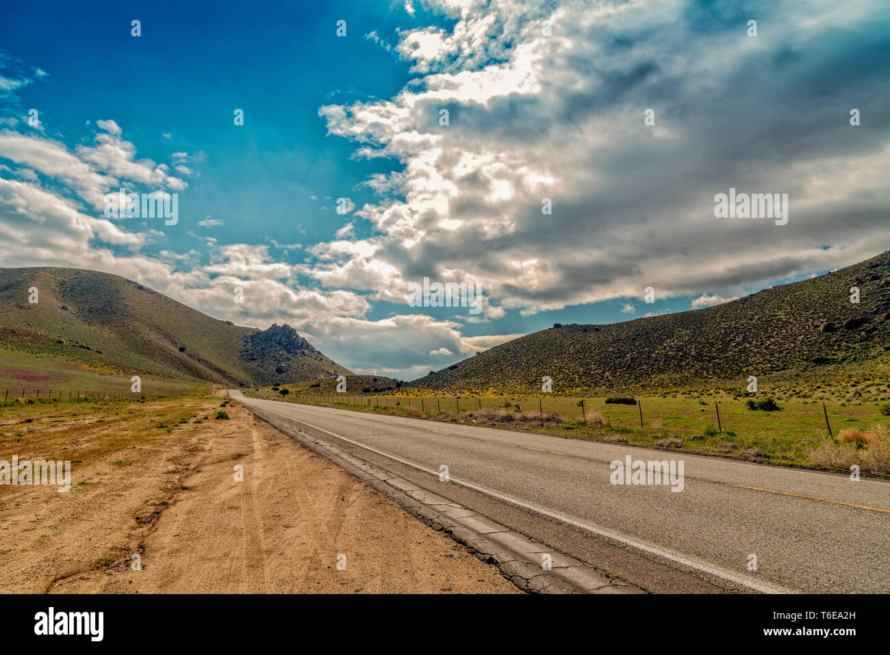 Roadside pull out looking at County road leading into mountains under bright blue sky with white fluffy clouds. Stock Photo