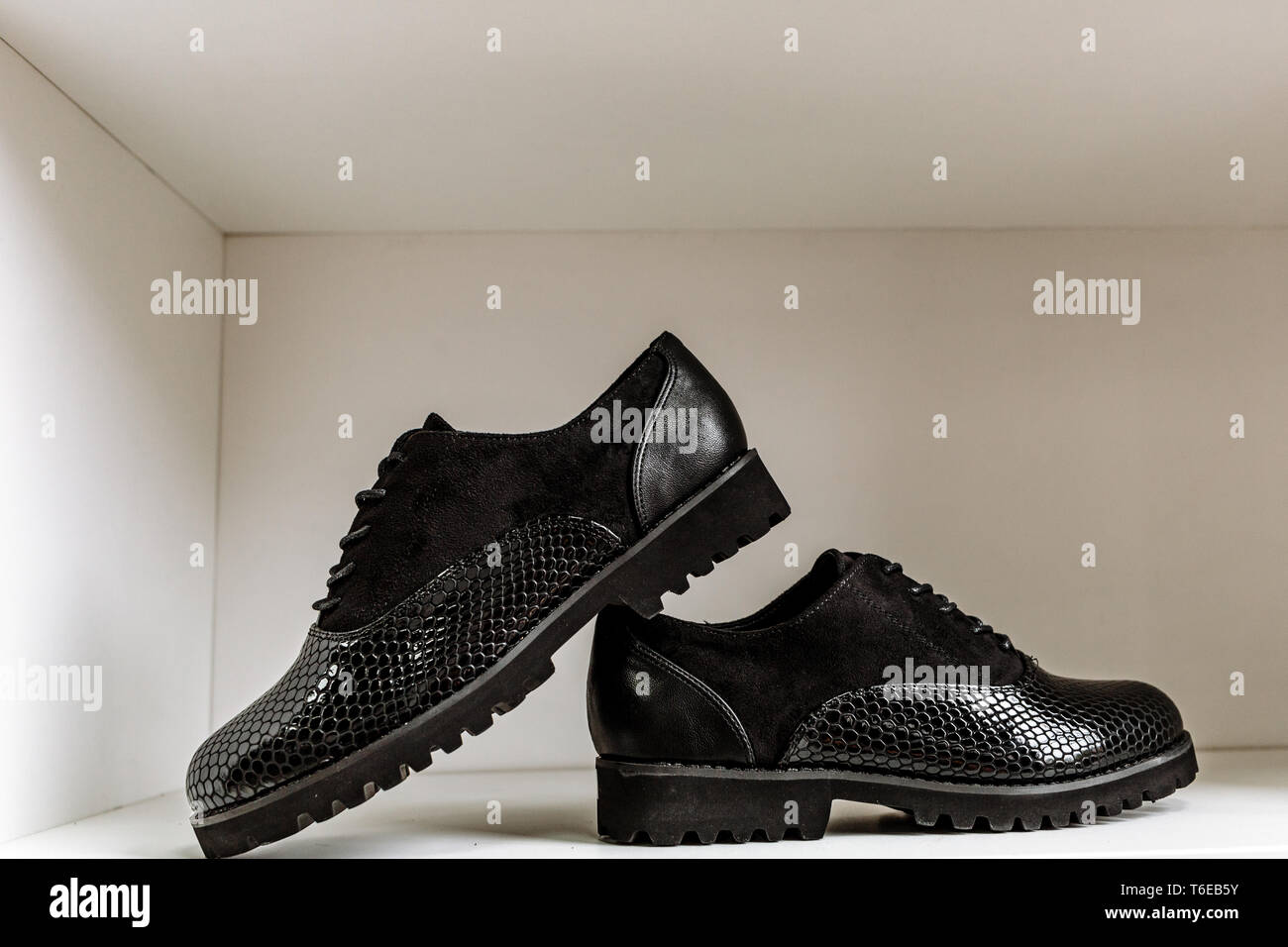 fashionable black patent leather shoes with a snake-skin pattern against a white shelf in the store Stock Photo