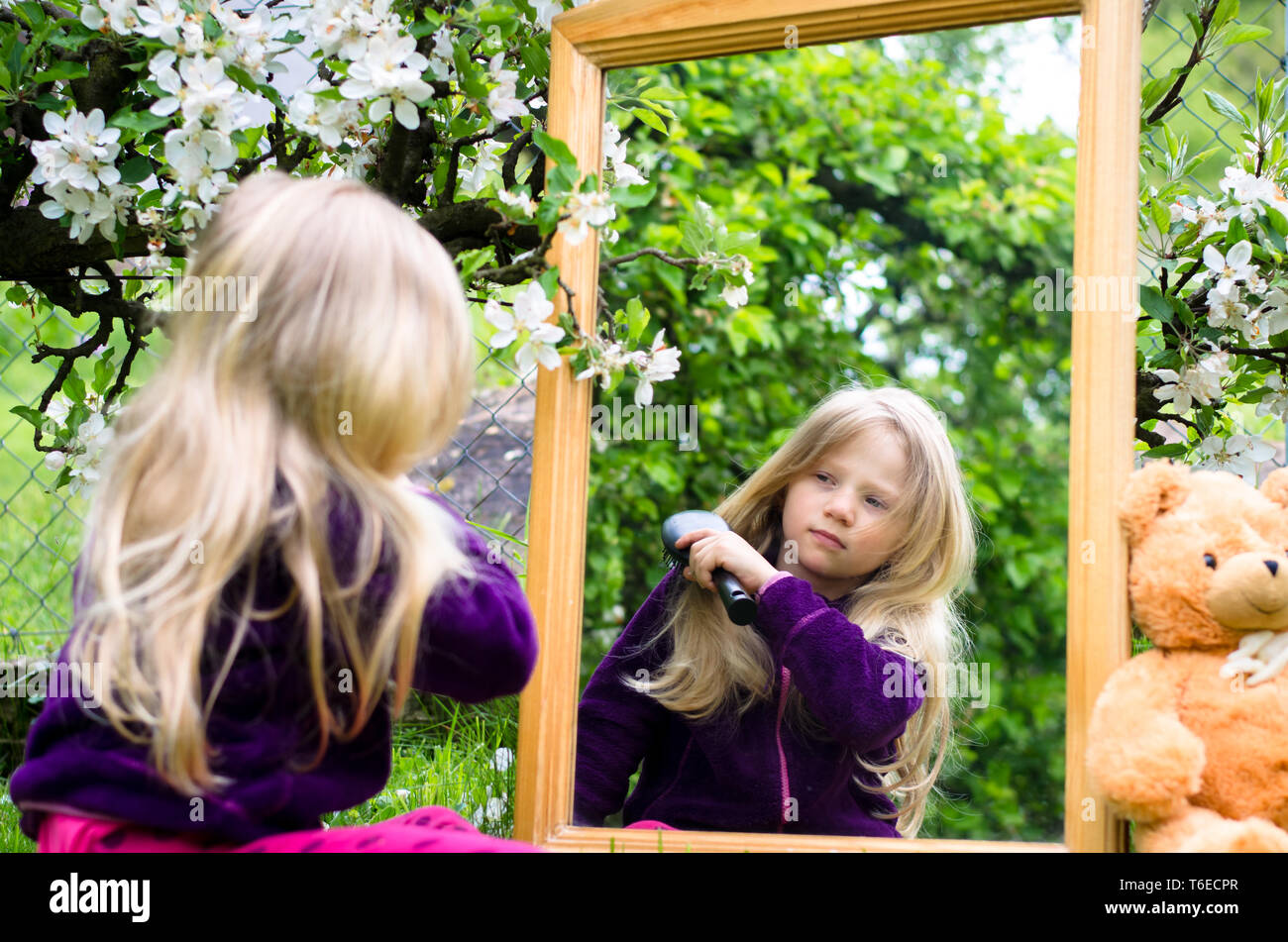 adorable blond girl brushing hair in front of the mirror Stock Photo