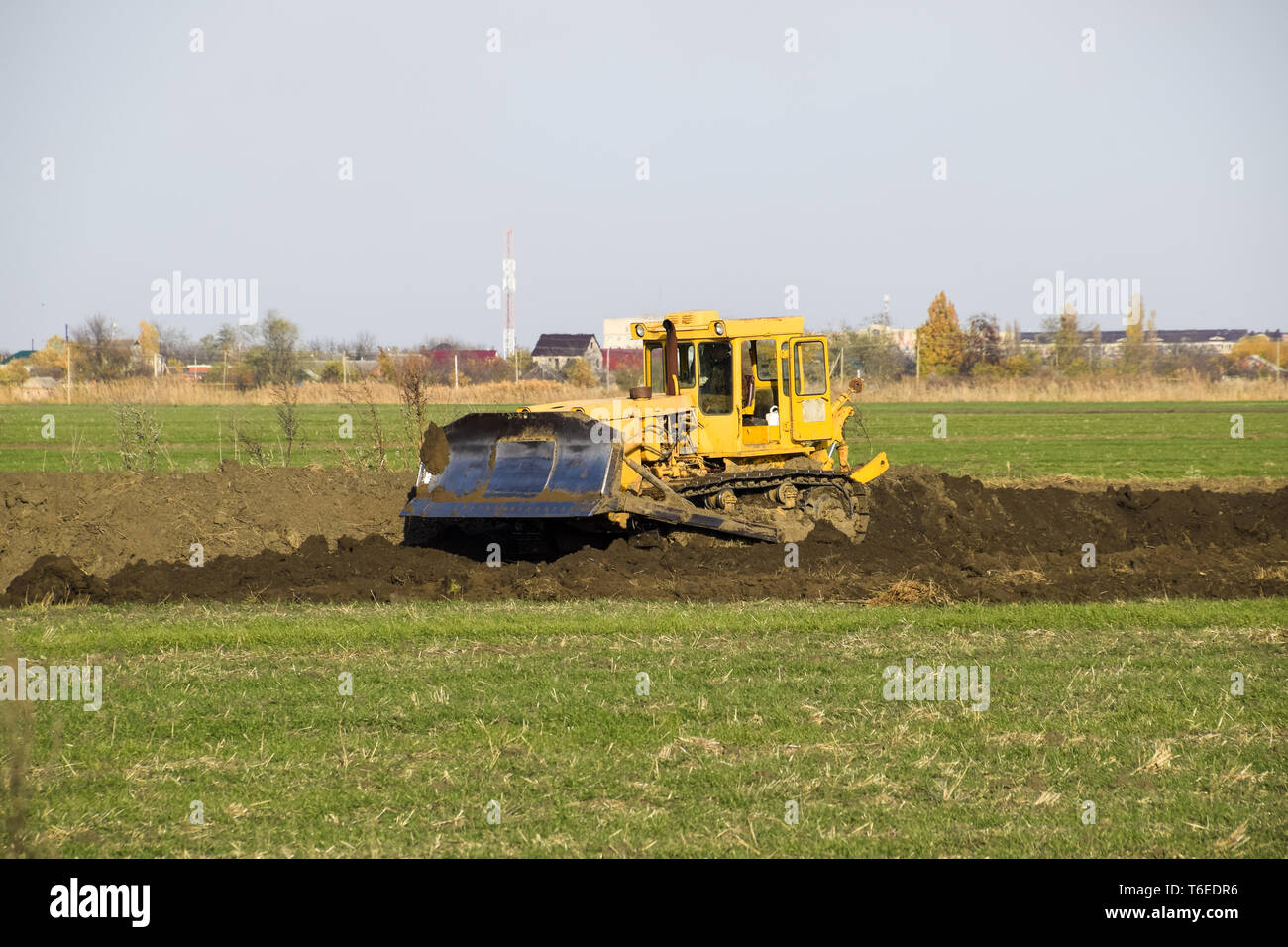 The yellow tractor with attached grederom makes ground leveling. Stock Photo