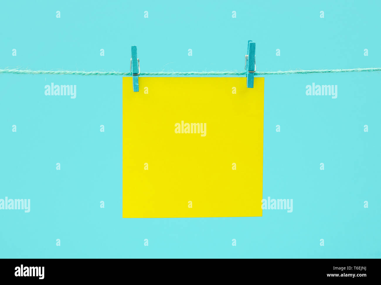Yellow empty paper sheet on the string with clothespins over blue background Stock Photo