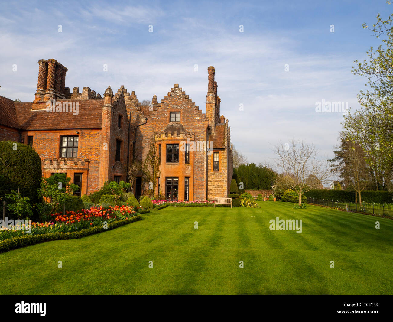 Chenies Manor House and Gardens in sunny April, showing orange colour schemed tulip borders, well maintained lawn, clipped hedges under a blue sky. Stock Photo