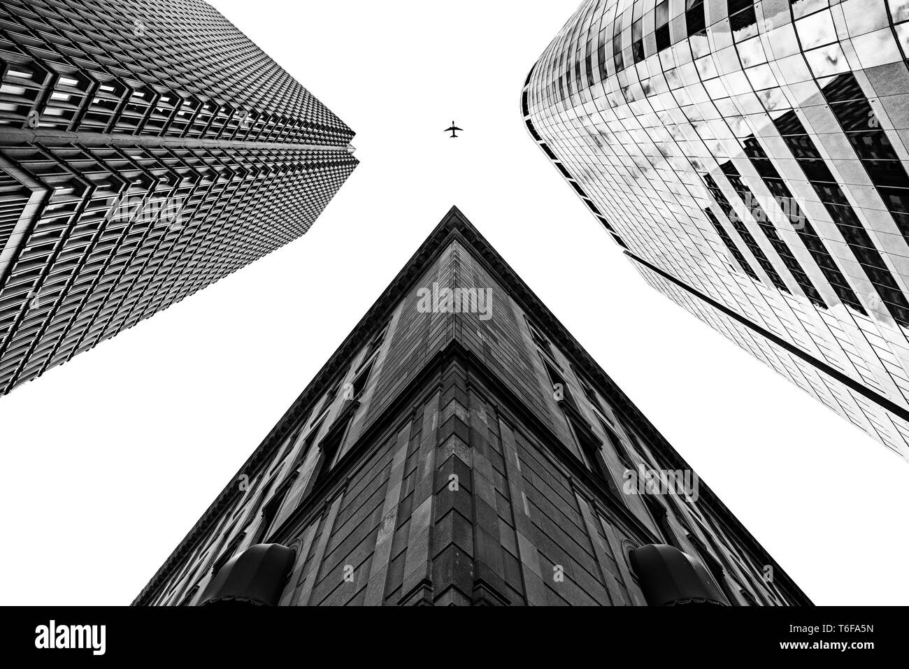 Three tall buildings shot from a low angle with an airplane in black and white Stock Photo