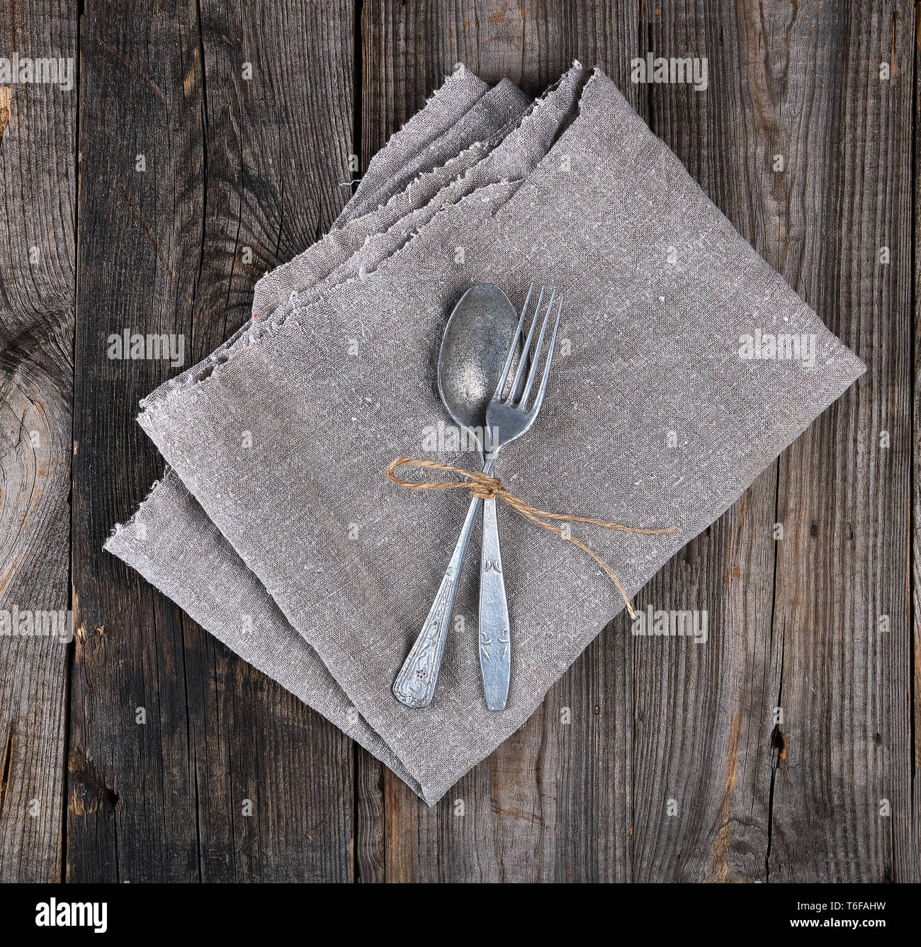 old metal fork and spoon tied with a brown rope on a gray linen napkin ...