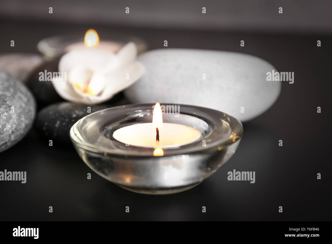 Burning candle and spa stones on black table Stock Photo