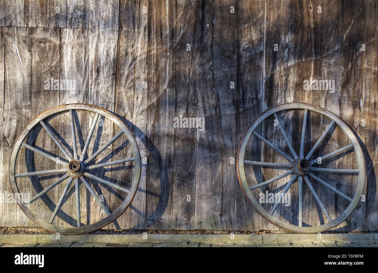 Two cartwheels lean against a barn wall Stock Photo