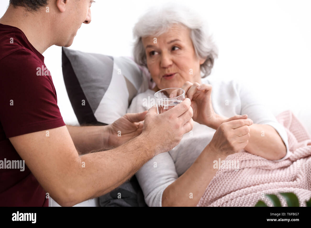 Man giving pills to elderly woman, indoors Stock Photo