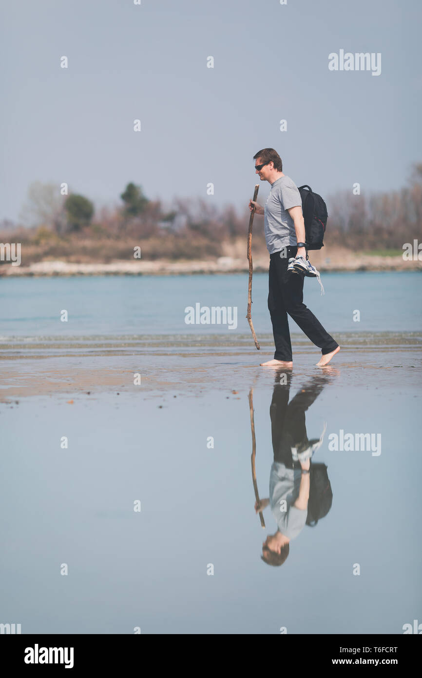 Water reflection of middle aged man walking on the beach Stock Photo