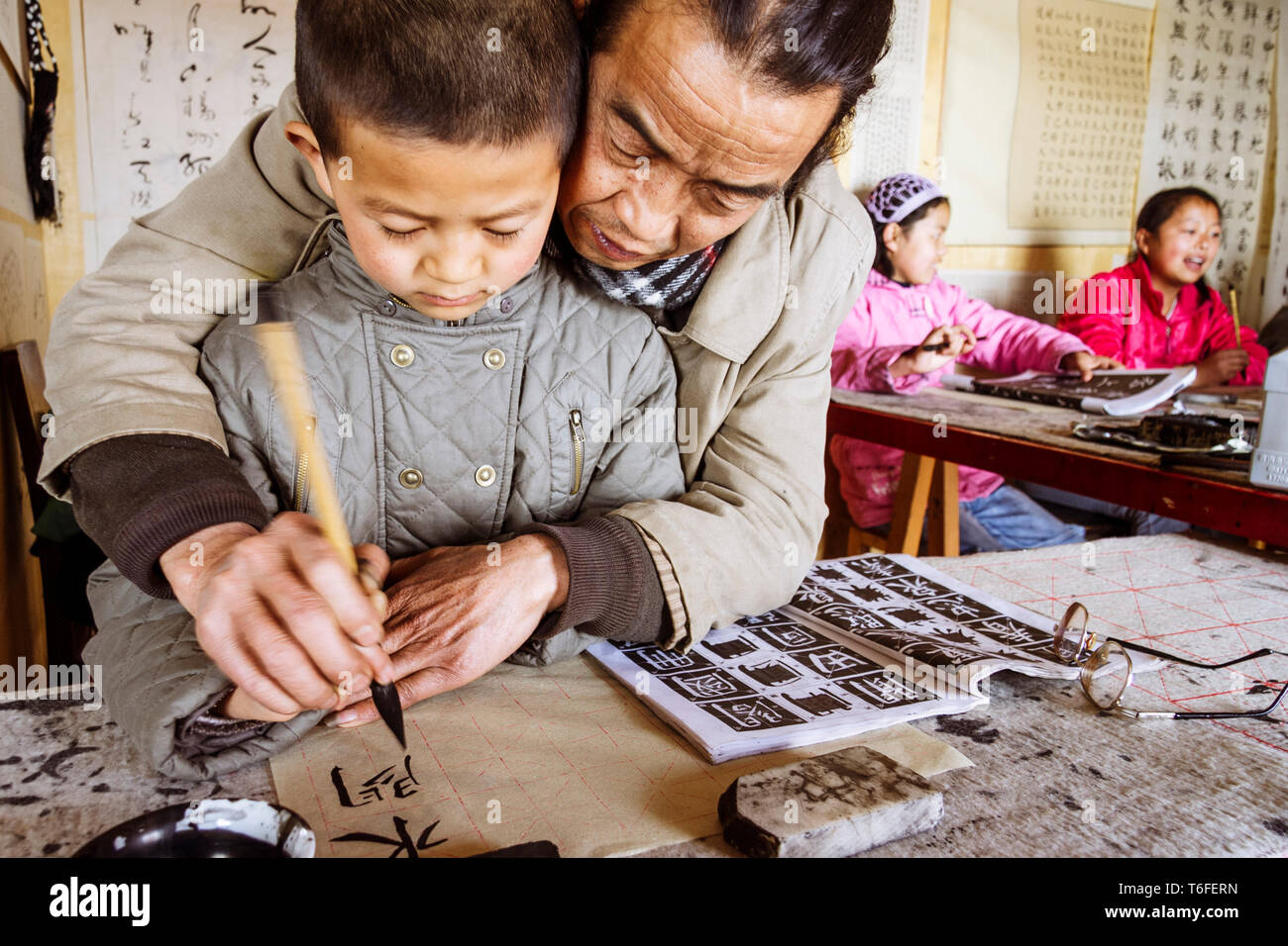 Lijiang, Yunnan province, China : A Chinese calligraphy teacher helps a pupil at a traditional calligraphy school in the Old Town of Lijiang, a nation Stock Photo