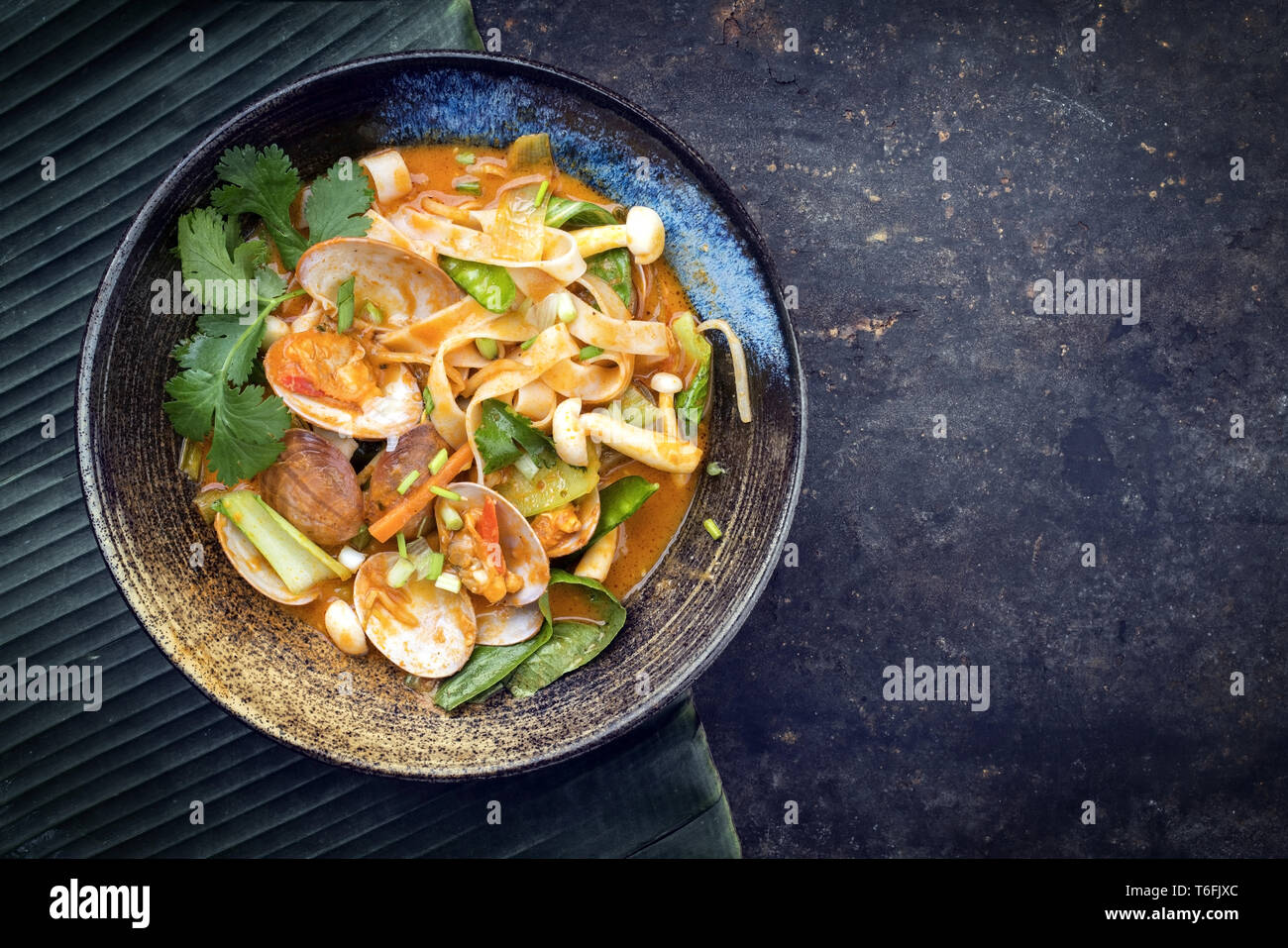 Traditional Thai kaeng phet red curry with clams and vegetable as top view in a bowl with copy space right Stock Photo