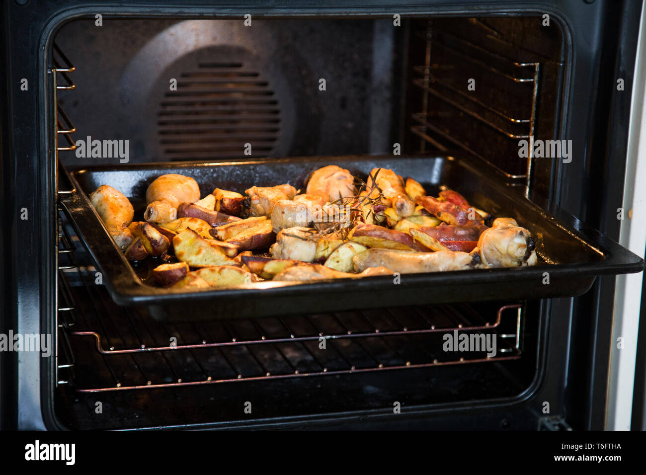Roasting dish in oven with roasted cooked chicken drumsticks and red