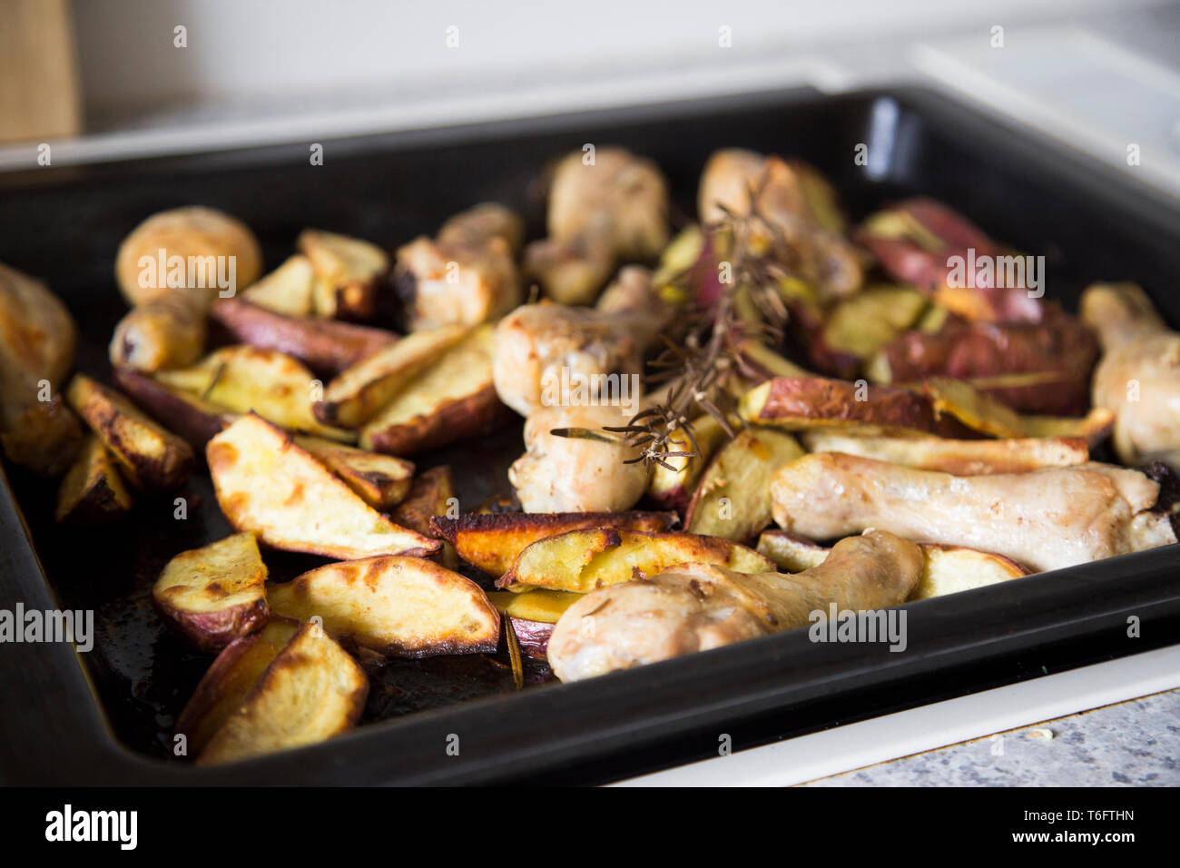 Roasting dish in oven with roasted cooked chicken drumsticks and red