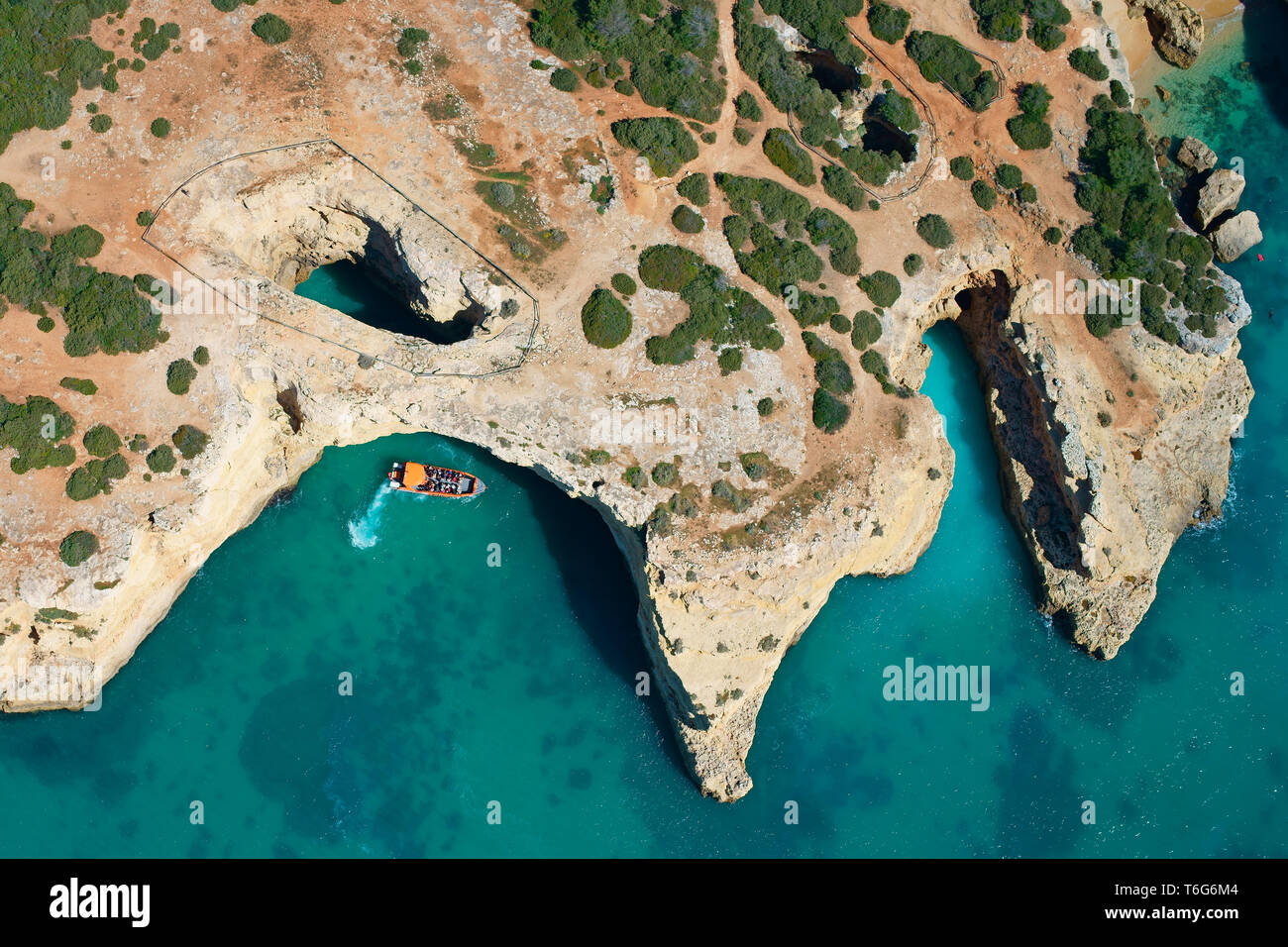 AERIAL VIEW. Sightseeing boat approaching a sea cave / sinkhole on the rocky coastline near Albandeira. Lagoa, Algarve, Portugal. Stock Photo