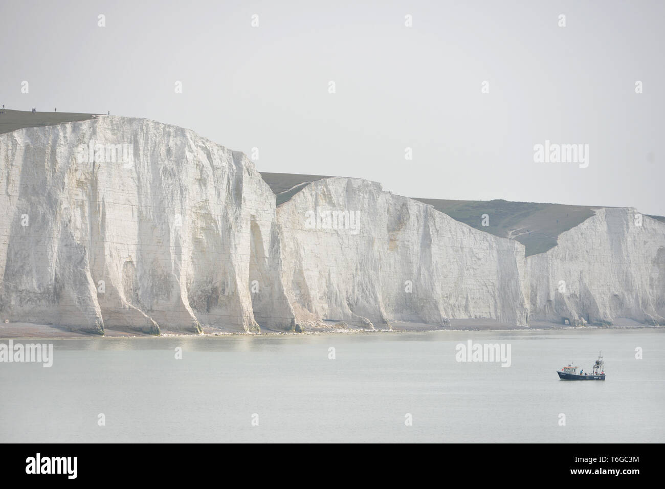 Cuckmere Haven, East Sussex, UK. 1st May, 2019. A small fishing boat working at the base of the iconic Seven Sisters chalk cliffs on overcast day near Eastbourne, Easy Sussex, on a flat hazy day. Credit: Peter Cripps/Alamy Live News Stock Photo