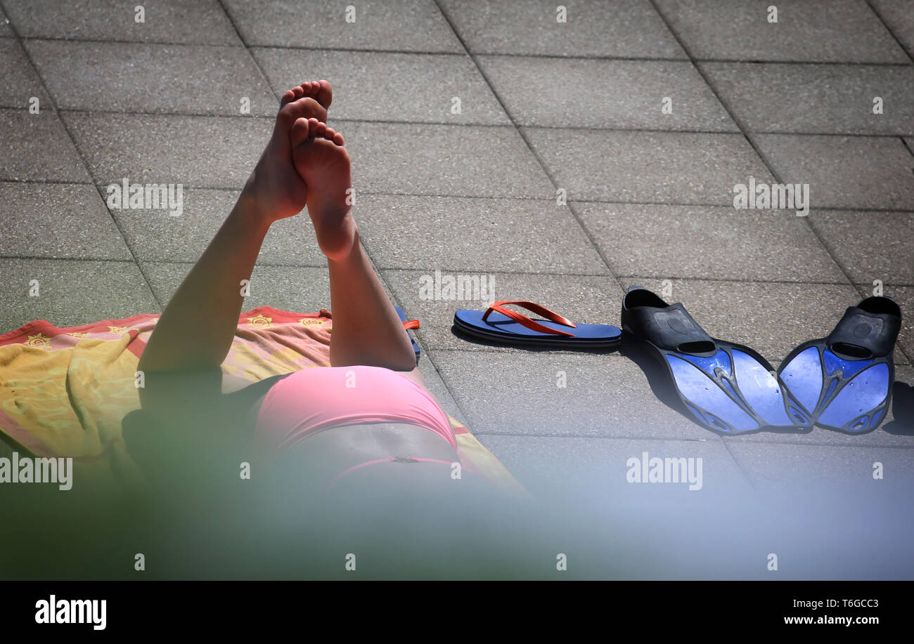 Landsberg Am Lech, Germany. 01st May, 2019. A young woman enjoys the sunshine at the edge of the swimming pool next to her flippers. The Landsberg Inselbad traditionally opens its bathing season on 1 May. Credit: Karl-Josef Hildenbrand/dpa/Alamy Live News Stock Photo
