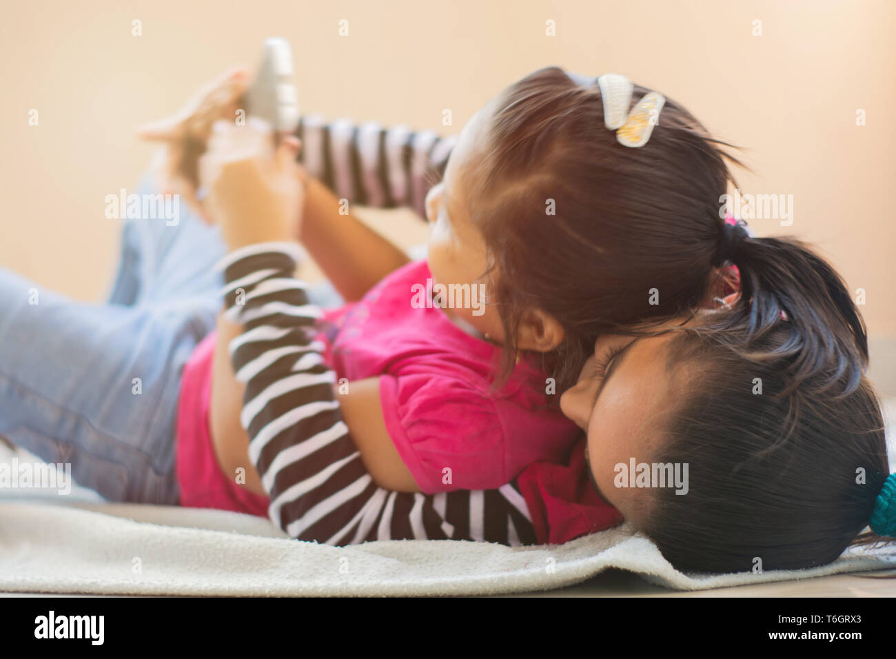 Two cute Indian litlle siblings fighting for Mobile phone, Crawling at each other on bed. Stock Photo