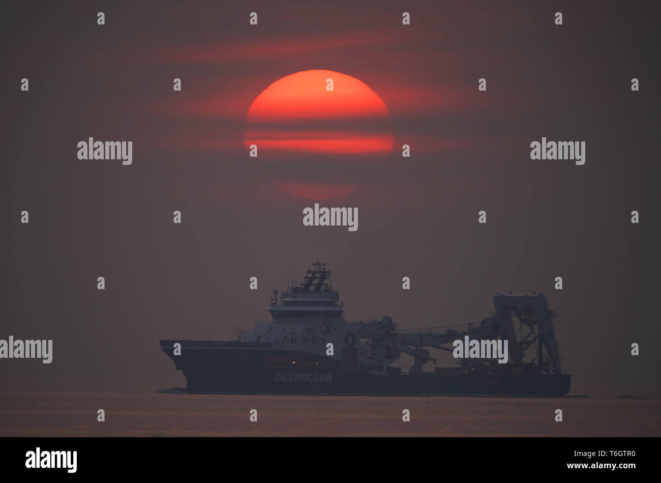 The sun rises through the mist at St Mary's lighthouse , Whitley Bay as the off shore supply ship Havila Phoenix heads into Blyth on the Northumberland coast. Stock Photo