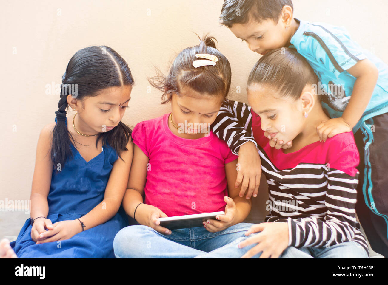 Group of four cute little Indian kids watching the single mobile device. Stock Photo