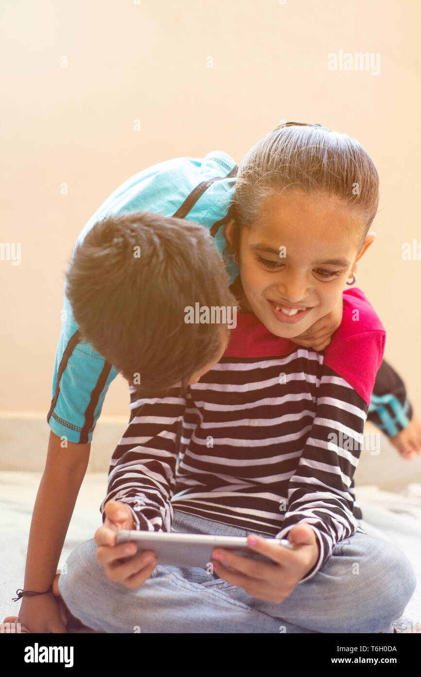 Two cute little Indian kids having fun by watching mobie device at home Stock Photo