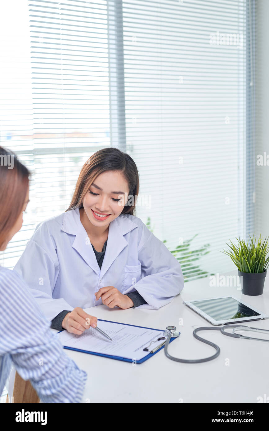 Female doctor talks to female patient in hospital office while writing ...