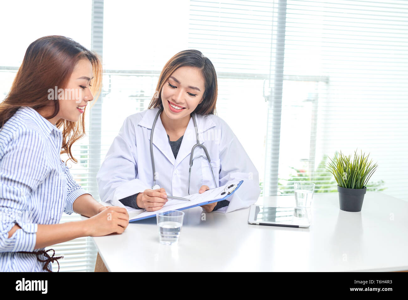 Female doctor talks to female patient in hospital office while writing ...