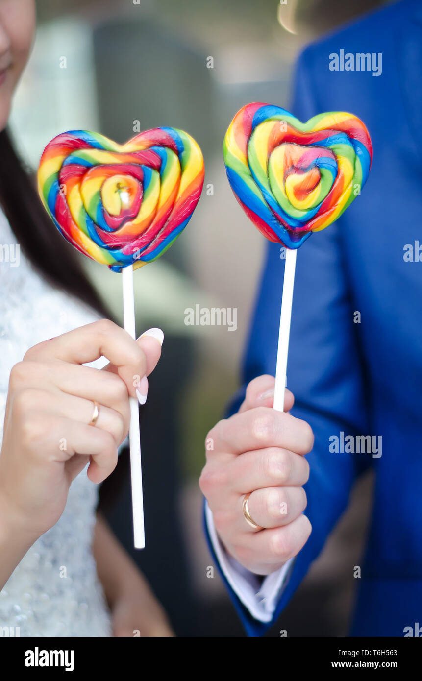 Sweet colorful candy hearts on sticks in the hands of the bride and groom Stock Photo