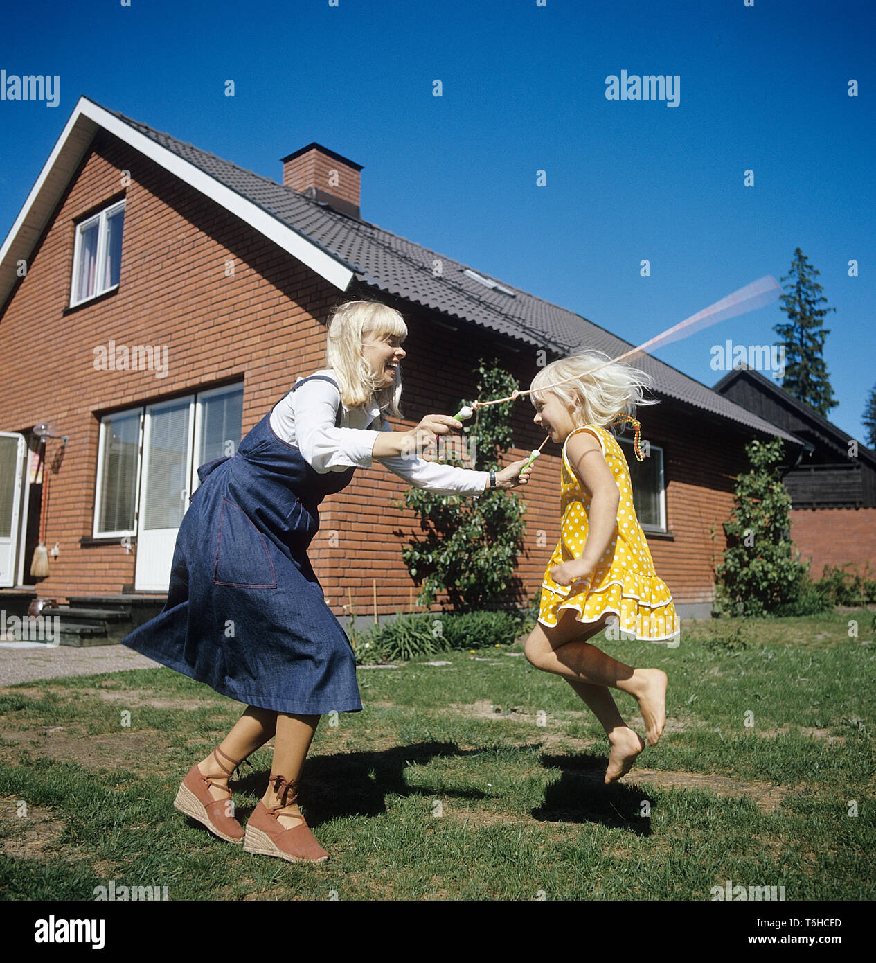 1970s lifestyle. A mother and her daughter is playing together in the garden. They are jumping rope together and laughing. Sweden 1970s. She is actress Margareta Sjödin. Stock Photo