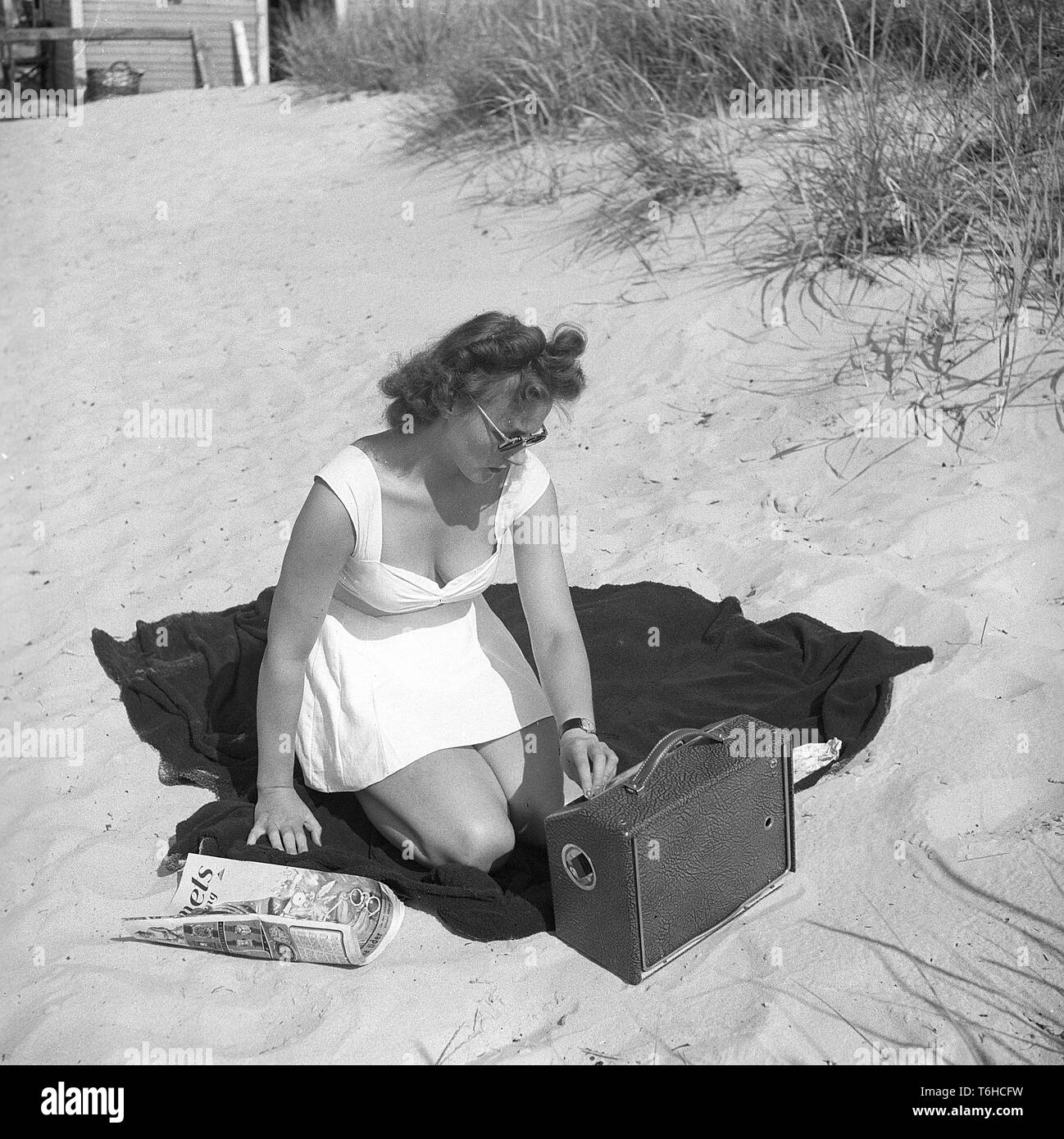 1940s woman on the beach. While the WW2 has hit Europe people are enjoying themselves on the beach of Falsterbo in Sweden. A young woman has brought along a battery operated radio and adjusts the reception on it to listen. The radio was the most important source of information about the war and everybody followed the news broadcasts. Sweden July 1941. Photo Kristoffersson ref 209-14 Stock Photo