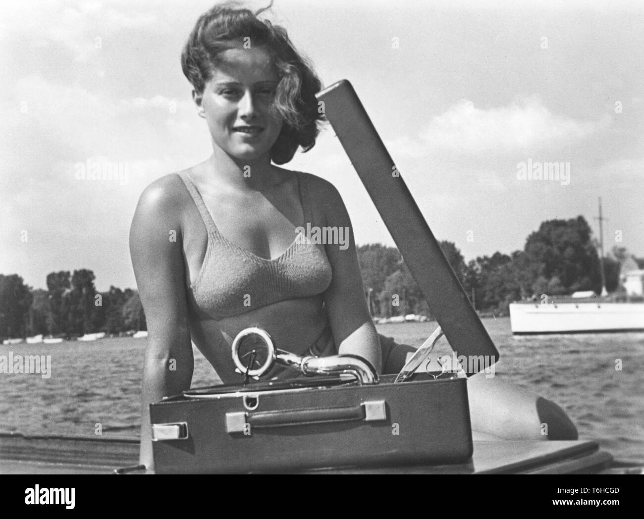 1940s summer lifestyle. A young woman with a portable gramophone player on a summer's day. It's operated by winding it up with a lever. The record then plays. When your hear that the recording begins to slow down, you know you have to wind i up again. The records were made of fragile material and the speed of the record to sound as it should was 78 revolutions per minute. Sweden 1940s. Stock Photo