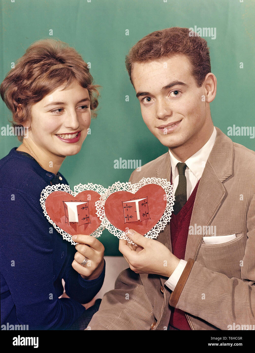 Couple of the 1950s. A young woman and man are each one holding heart shaped papers colored in red with ornaments around it. An illustration for Valentine's day. Sweden 1950s. Stock Photo
