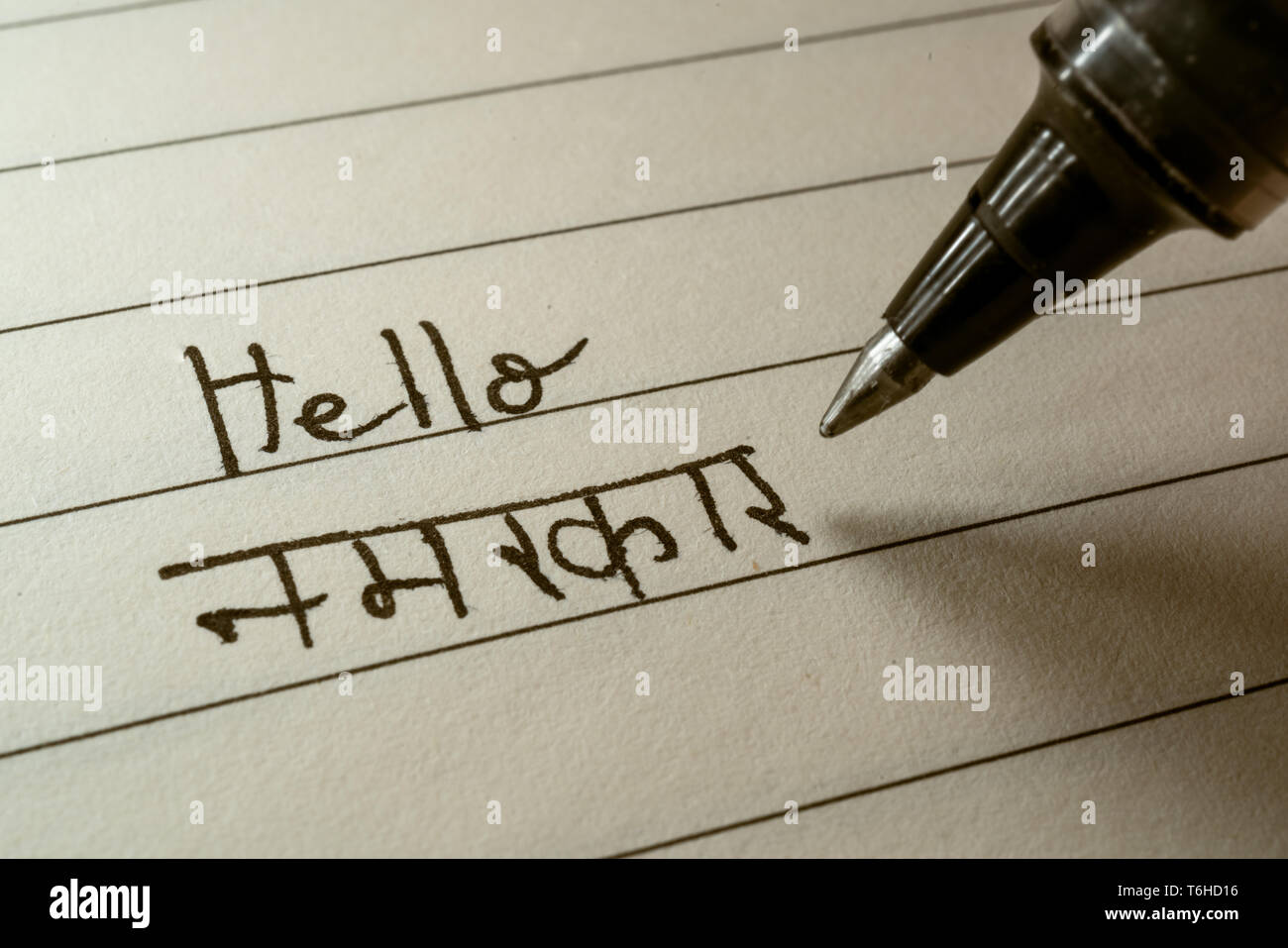 Beginner Hindi language learner writing Hello Namaste word in Indian Hindi alphabet on a notebook close-up shot Stock Photo