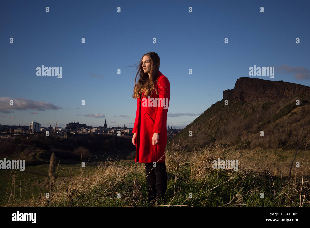 Young woman in long red jacket standing in a park in Edinburgh Stock Photo