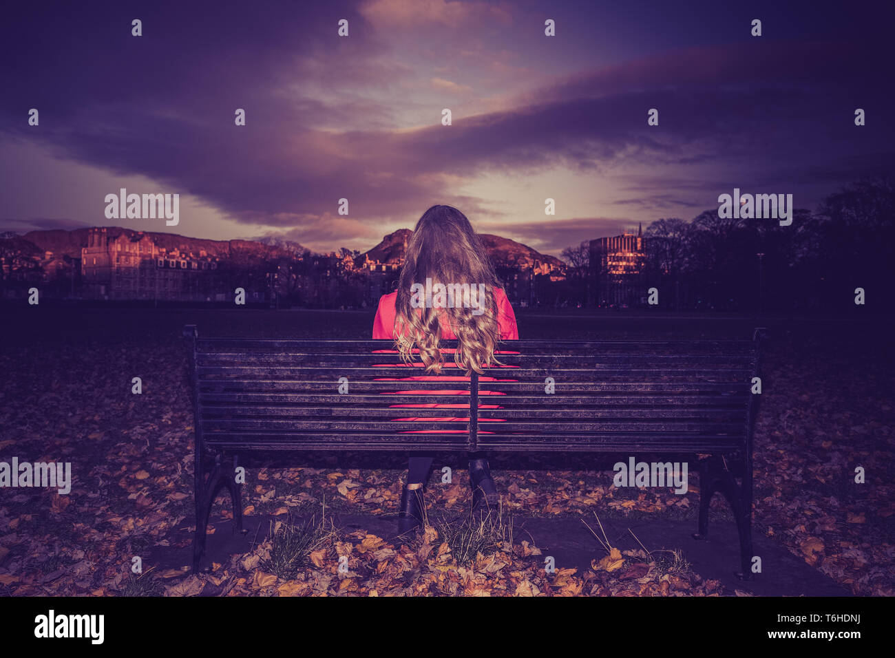 Young woman all alone on a bench in a park at sunset. Stock Photo