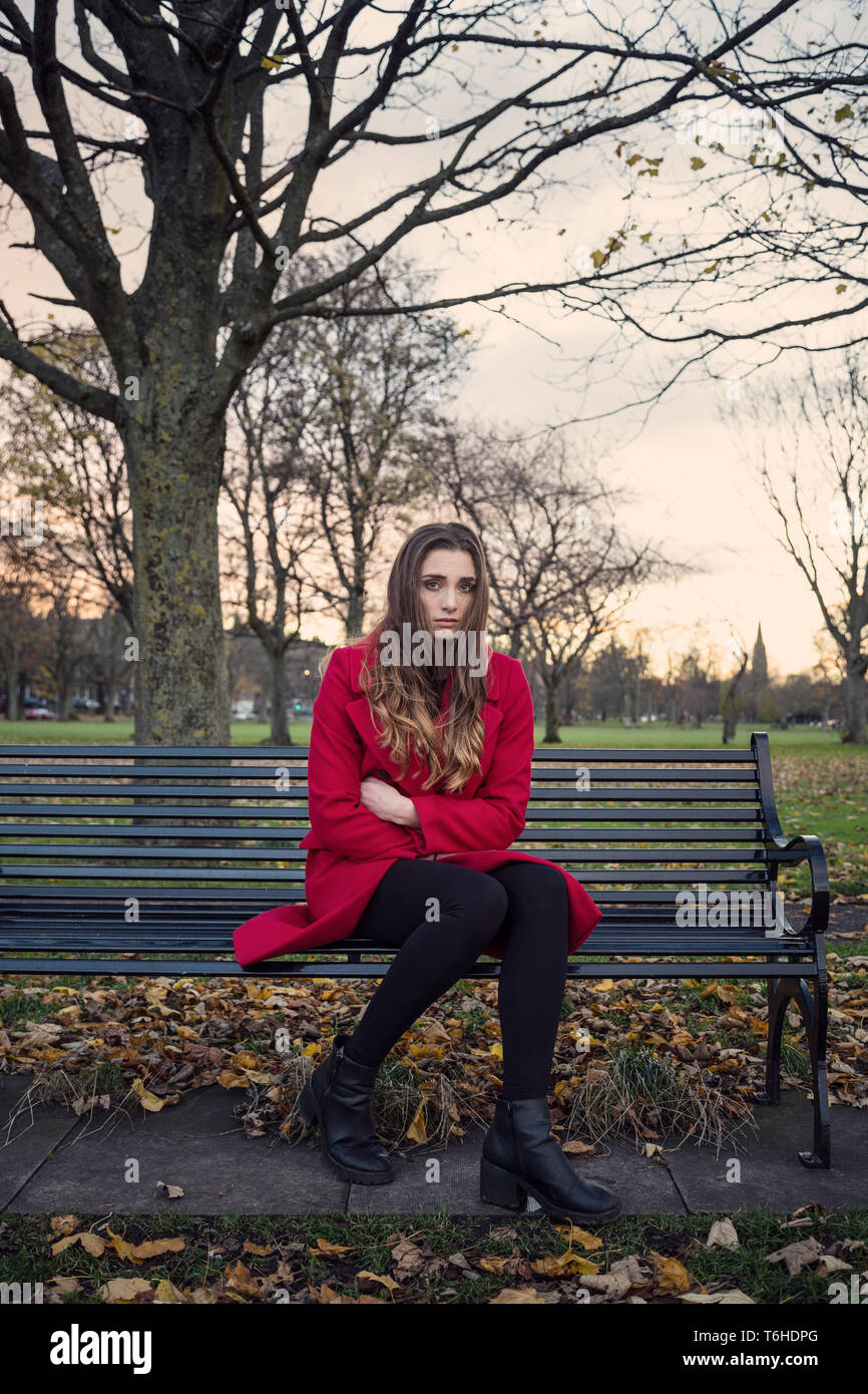 A young woman sitting on a bench in a park, with lots on her mind, feeling isolated and anxious. Stock Photo