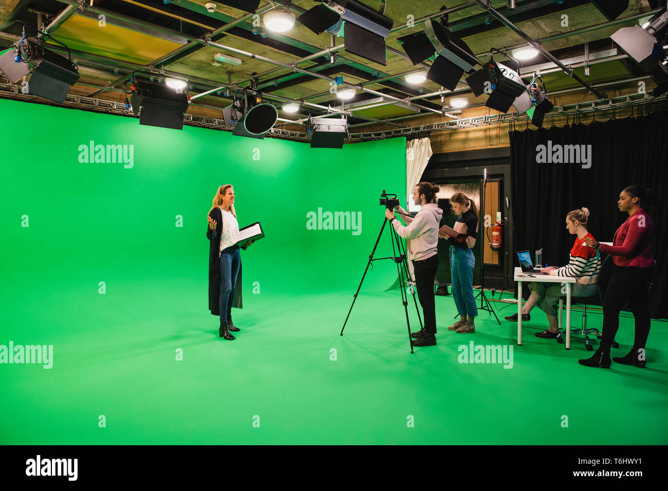 A wide-angle shot of a multi-ethnic group of people working in a film studio, a mature caucasian woman can be seen presenting in front of a green scre Stock Photo