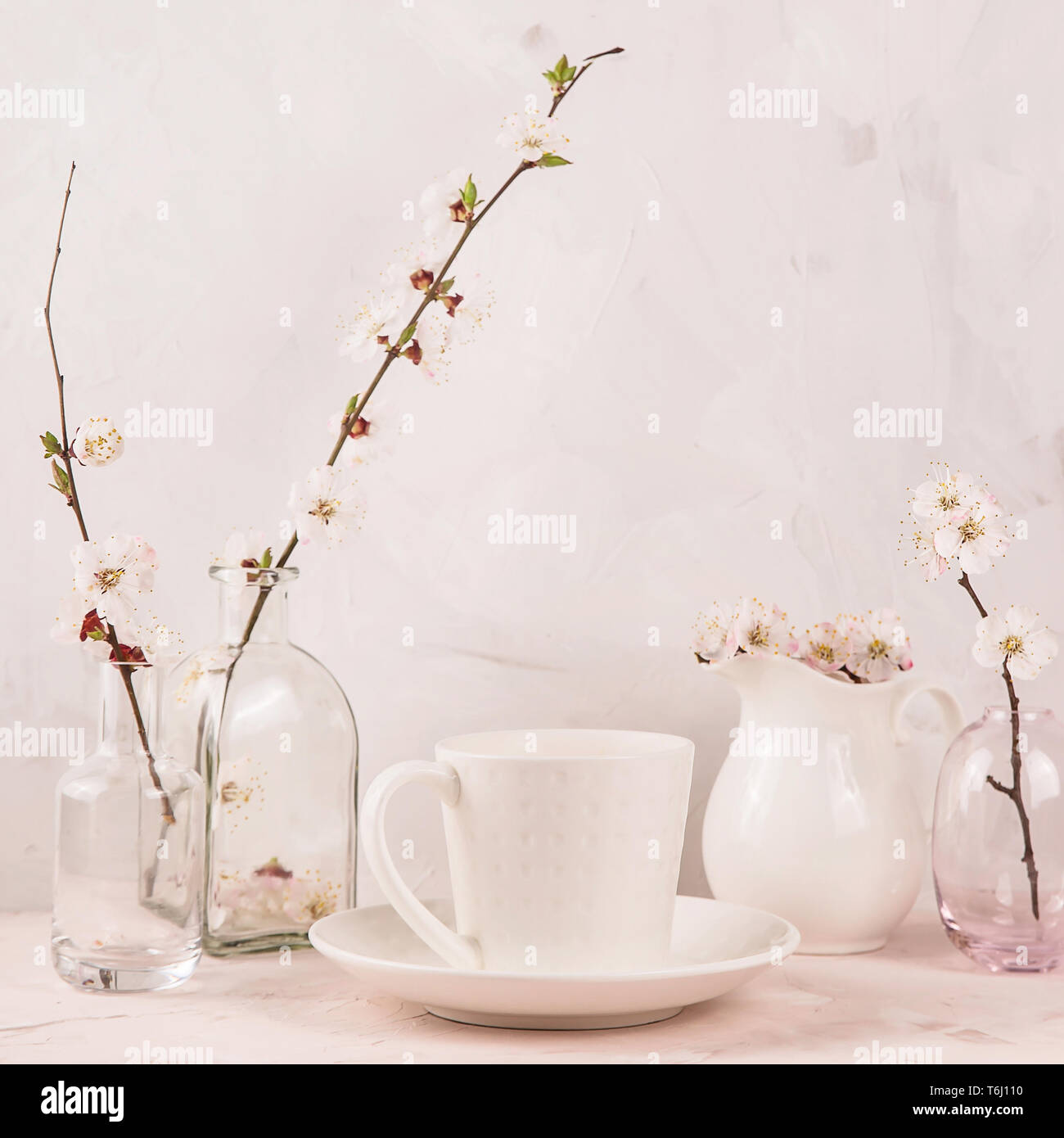 A Stylish White Cup Of Coffee Among Small Vases With Spring