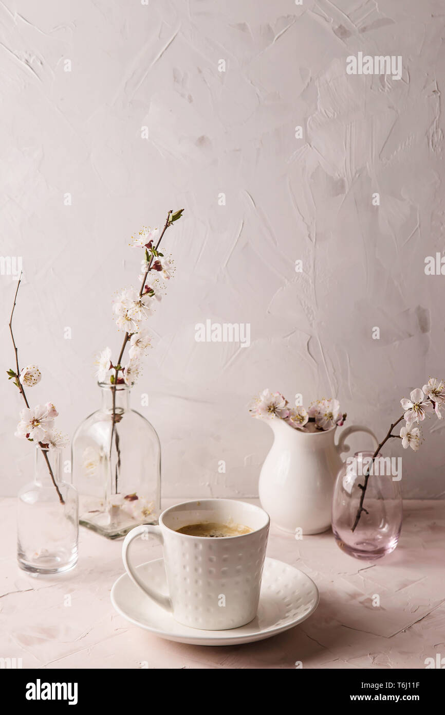 A Stylish White Cup Of Coffee Among Small Vases With Spring