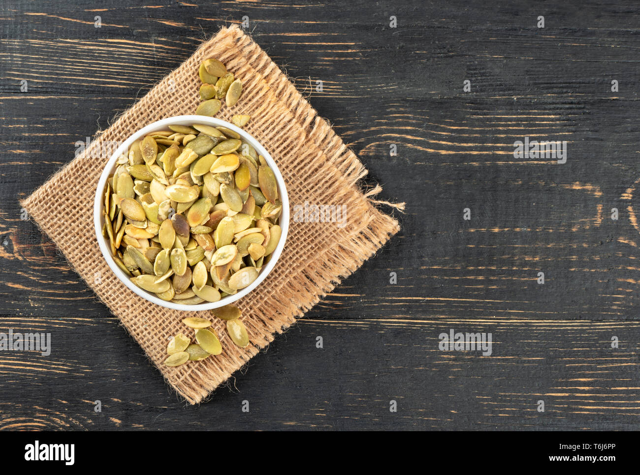Pumpkin seeds without shell in a bowl on burlap and empty wooden